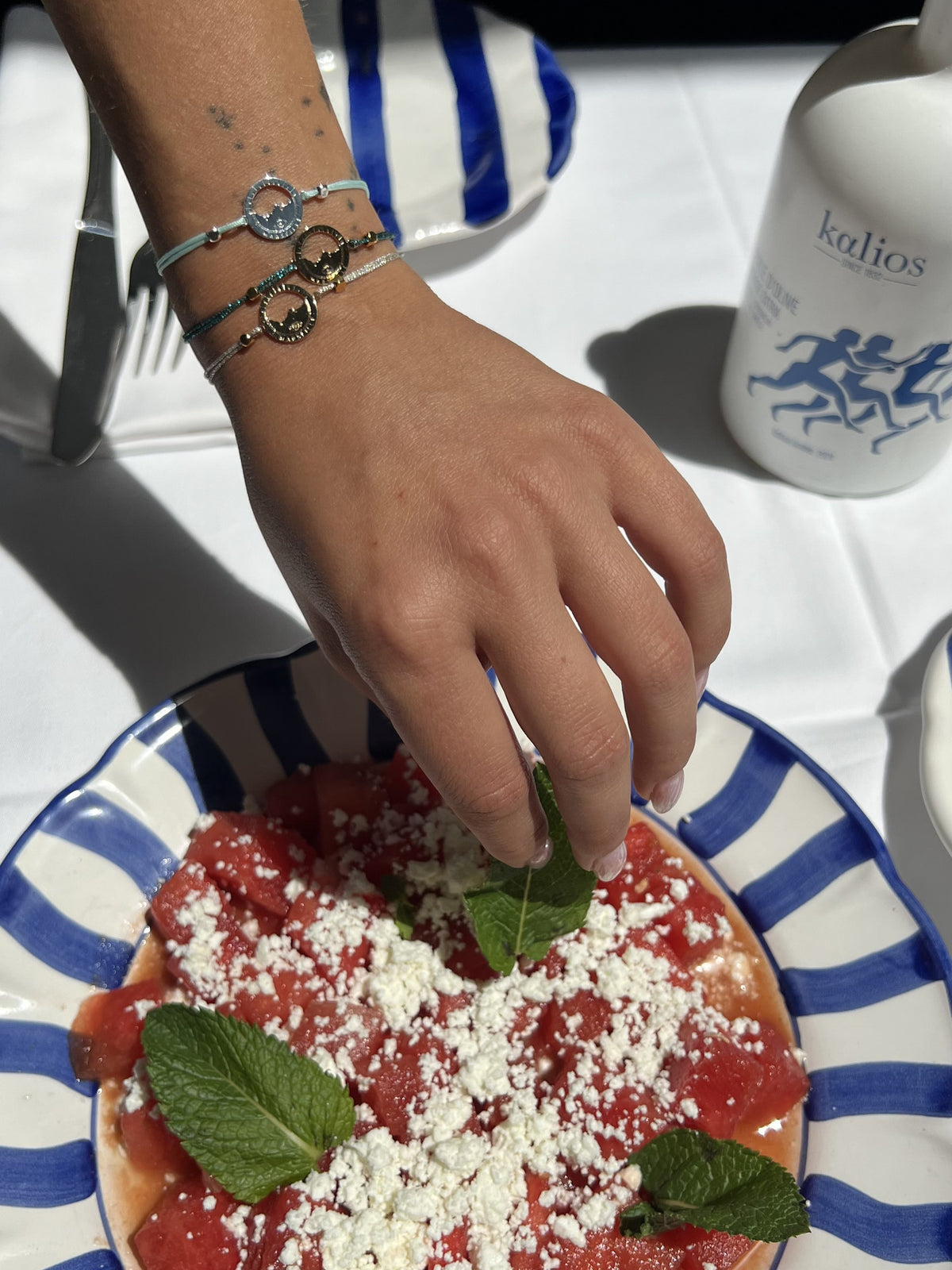 Bracelets Les Catalans cordon nylon portés en superposition, médaille Marseille ajourée plaquée argent et médailles dorées, table d'été à Marseille — Ligne Bleue