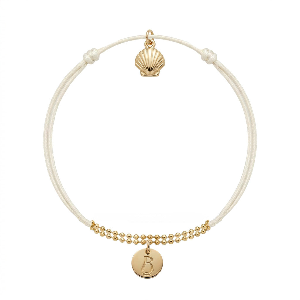 Bracelet Le Vallon des Auffes doré à l'or fin, cordon écru, médaillon au monogramme LB devant et coquille Saint-Jacques au creux du poignet — Ligne Bleue, Marseille