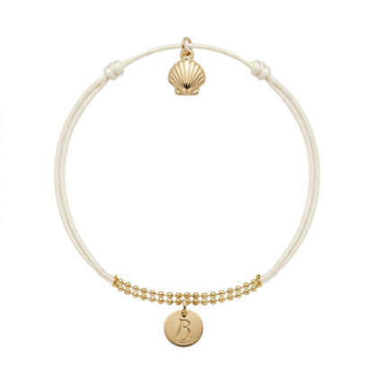 Bracelet Le Vallon des Auffes doré à l'or fin, cordon écru, médaillon au monogramme LB devant et coquille Saint-Jacques au creux du poignet — Ligne Bleue, Marseille